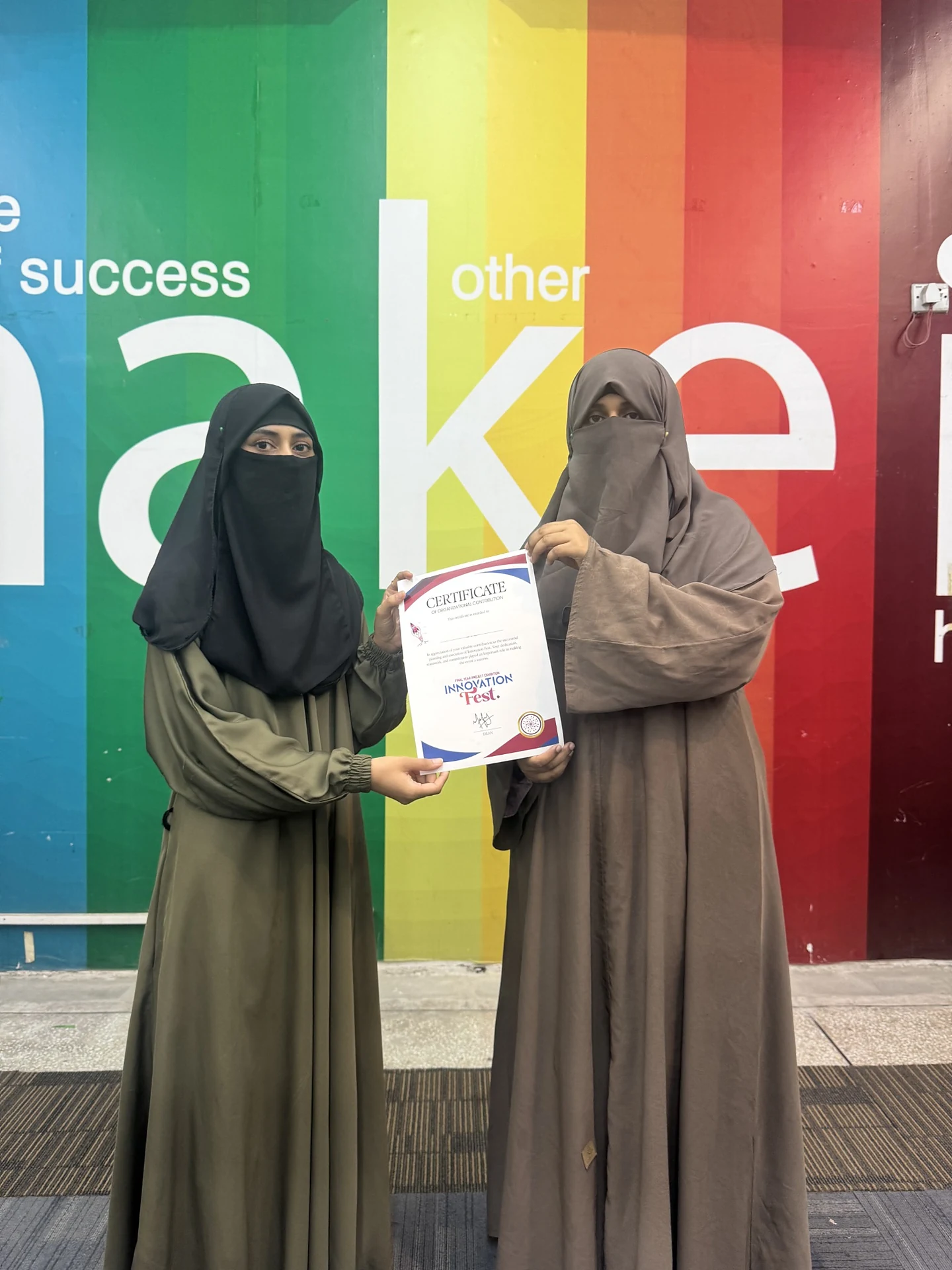 Two women holding a certificate together in front of a colorful wall.