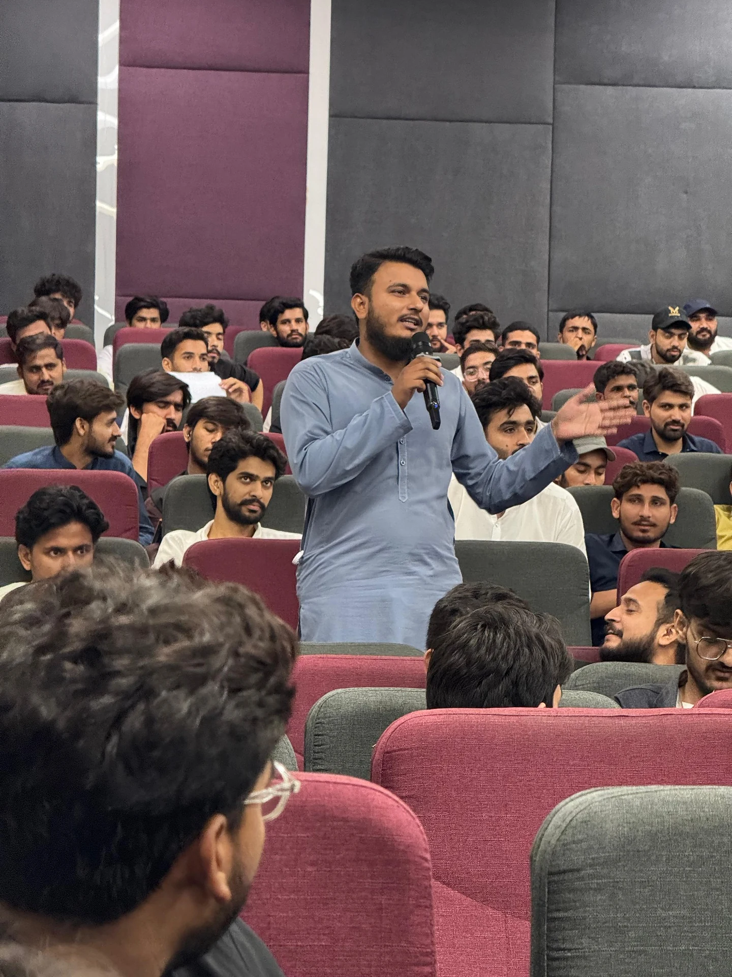 An attendee speaking into a microphone during a session in an auditorium.