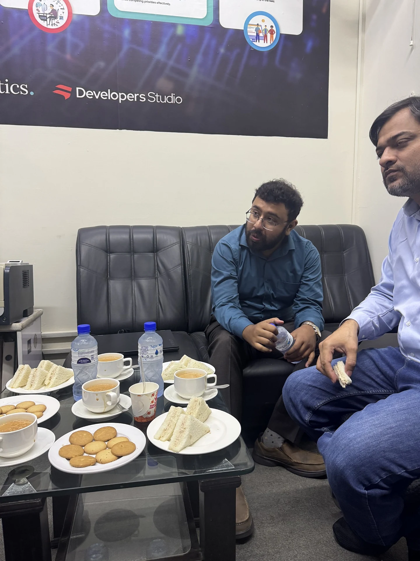 Two people talking in an office lounge area beside refreshments.