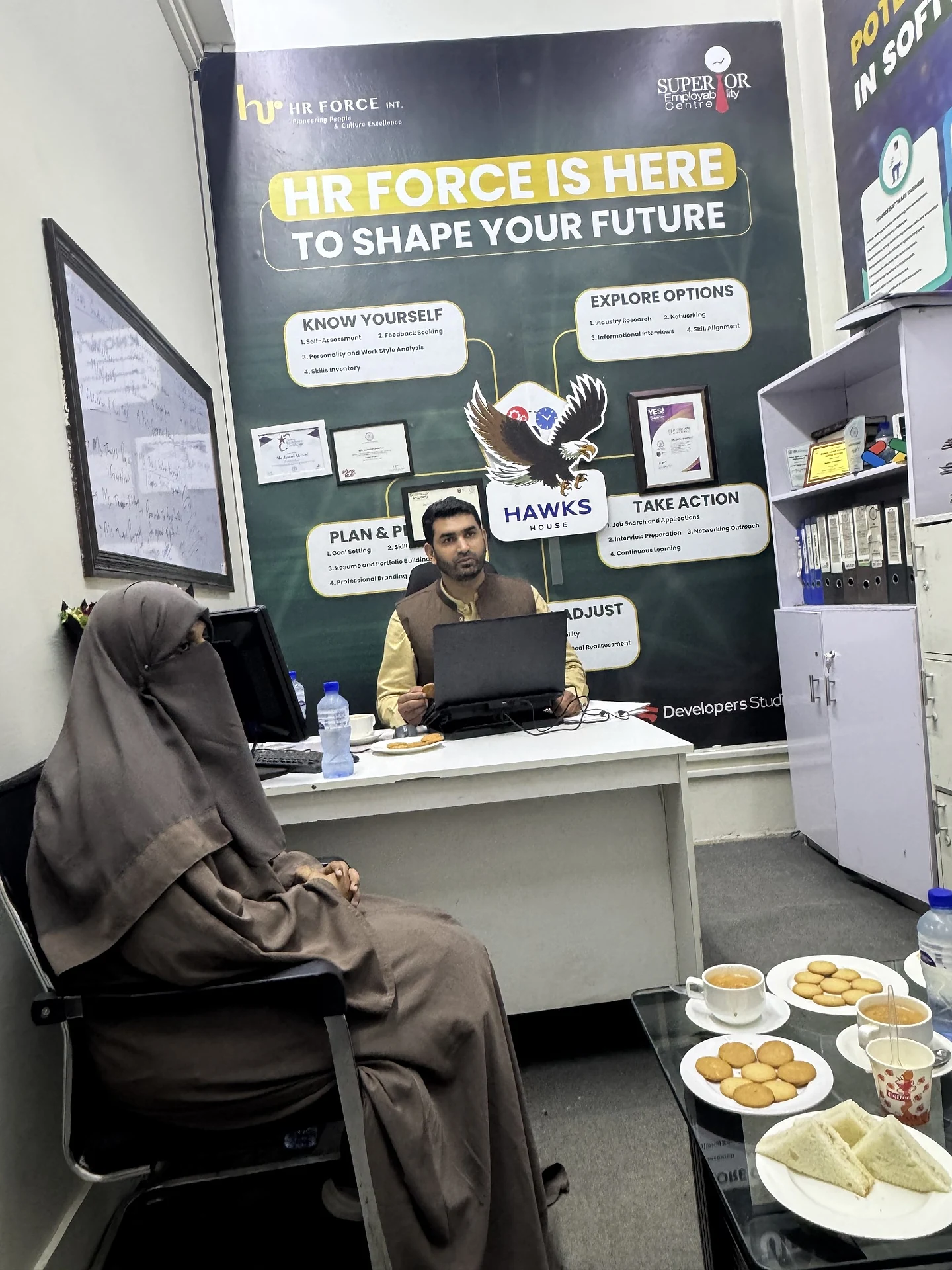 A facilitator speaking from a desk during a session in an office room.