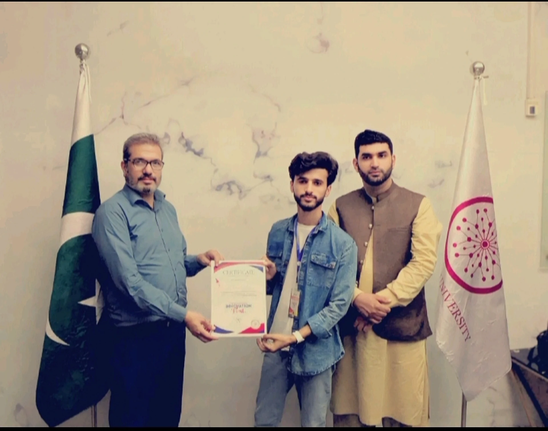 A student holding a certificate beside two presenters during a formal photo.